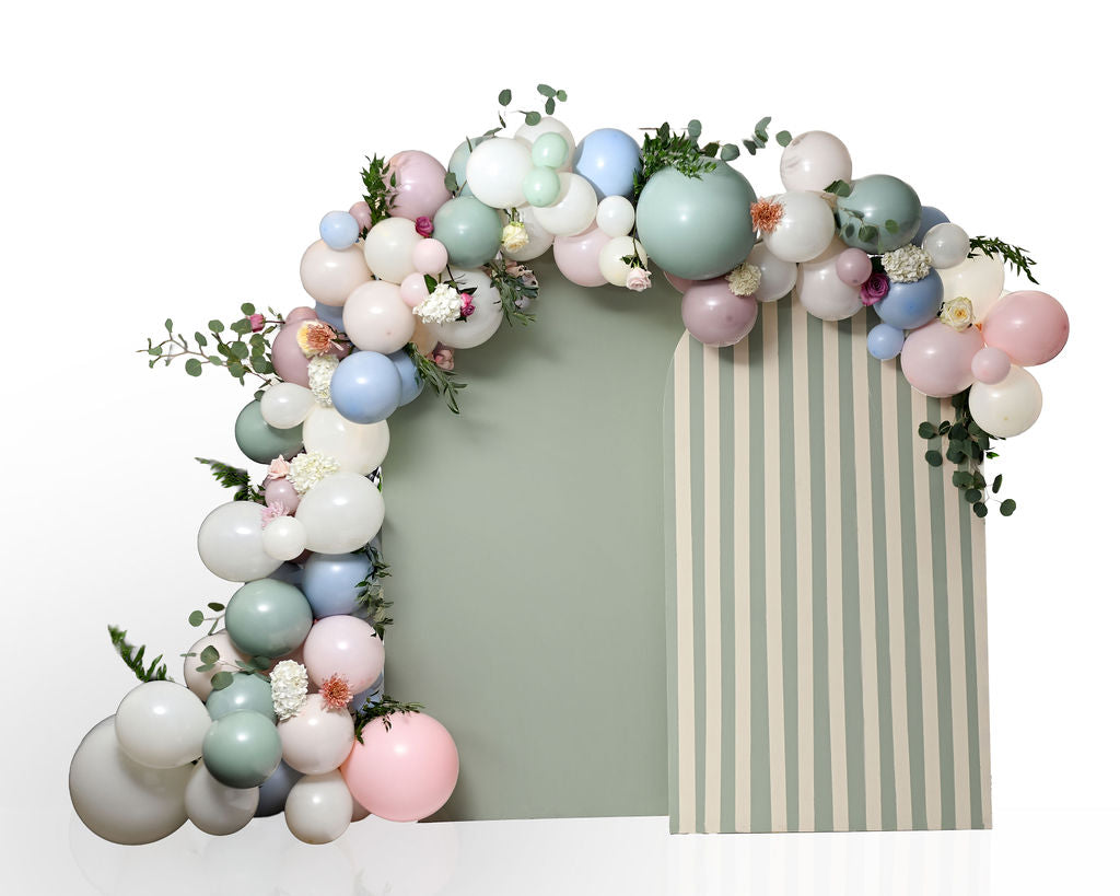Pastel balloon garland arch with eucalyptus greenery and fresh flowers, arranged over a sage green and cream striped arch backdrop.