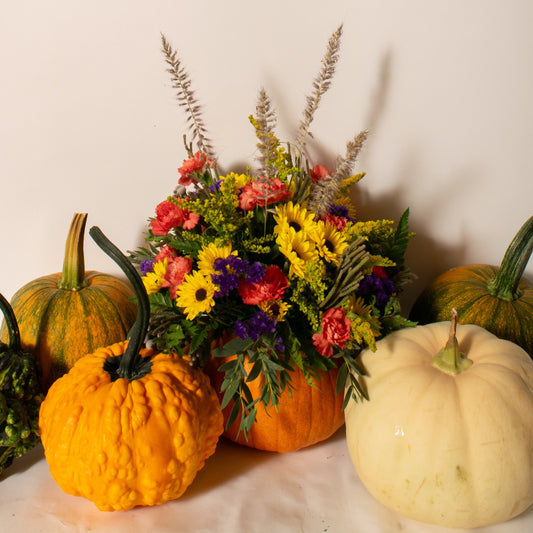 Decorative arrangement of pumpkins and a floral bouquet on a light background