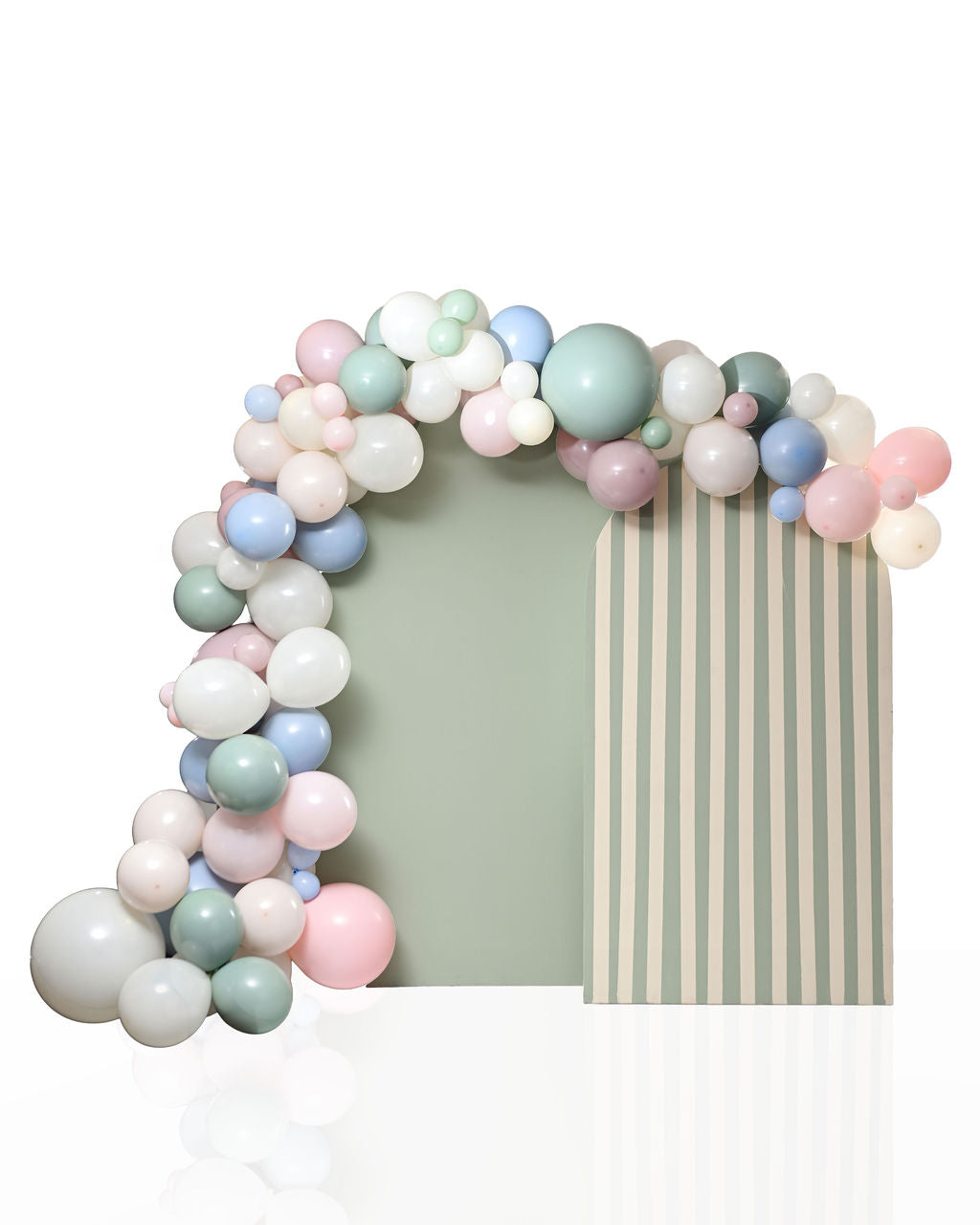 Pastel balloon garland arch in sage green, dusty pink, cream, and dusty blue with a hint of greenery, viewed at a slight angle over a two-tone arch backdrop — solid sage green on the left panel and cream-and-sage stripes on the right.