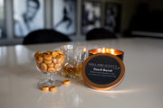 Lit Holland Scents Dutch Barrel soy candle beside a bowl of butterscotch candies and a glass of bourbon, Pella, Iowa