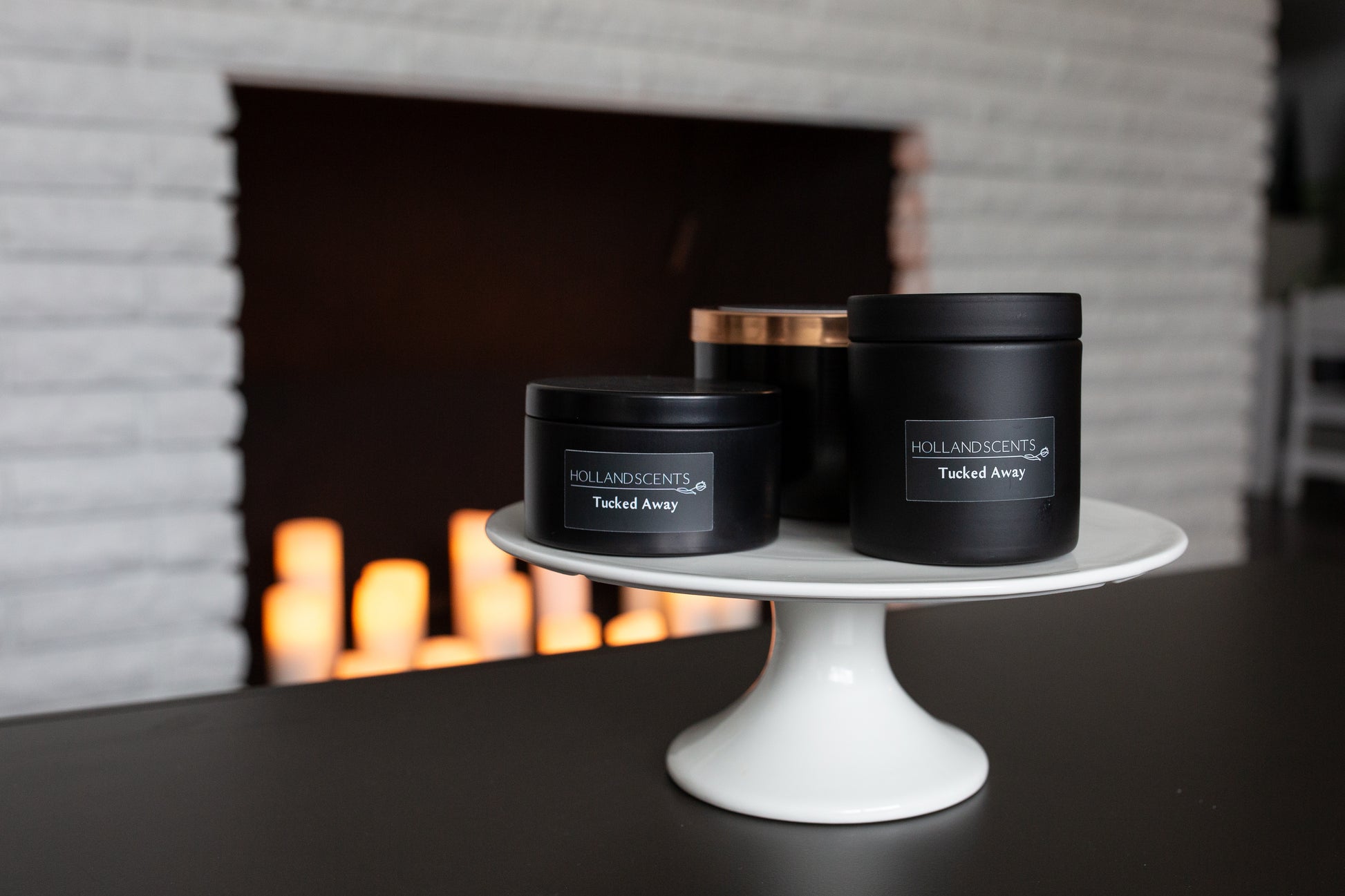Holland Scents Tucked Away soy candle in three sizes displayed on a cake stand, Pella, Iowa
