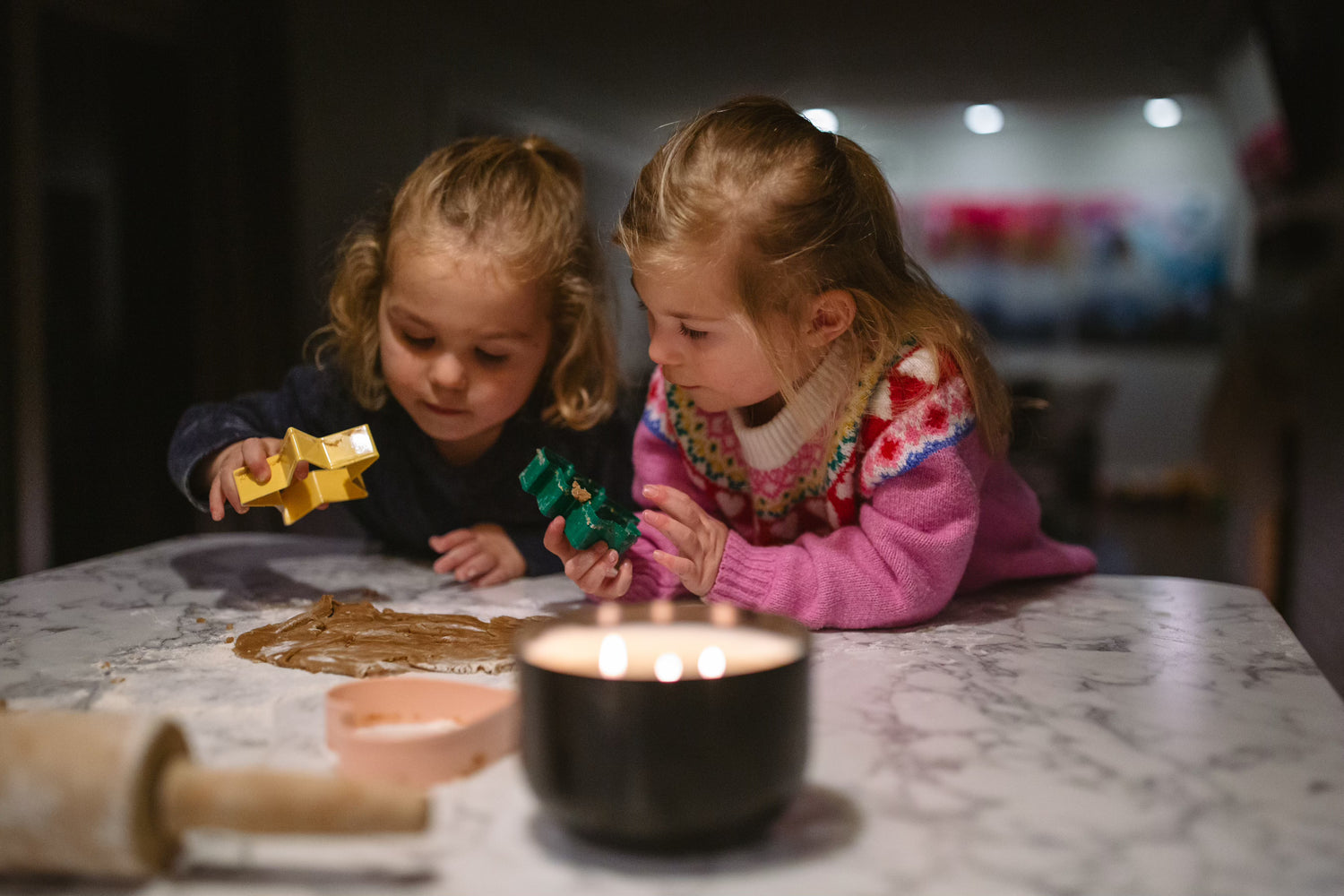 Kids decorating gingerbread cookies at a kitchen counter with a Holland Scents candle nearby. Candle hand poured in Pella, Iowa. 